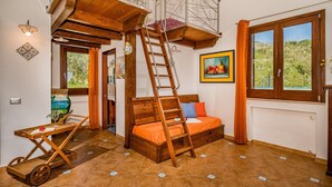 Ein Schlafzimmer im Loft-Stil mit einer Holzlade, einem Bett, einem kleinen Tisch und Blick auf Grün durch das Fenster.