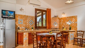 Eine Küche mit gefliestem Spritzschutz, Holzschränken, einem Kühlschrank, einem Esstisch mit Stühlen und einem Fernseher über dem Kühlschrank.