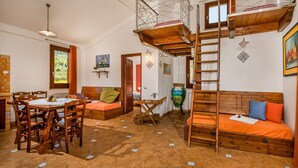 Ein rustikaler Raum mit Holztisch, einer Couch, einem Schlafplatz in der Schlaffküche und einer Leiter.