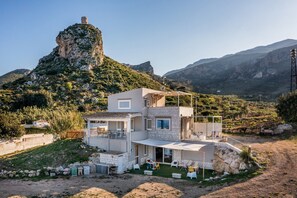 A modern two-story house with a patio area, surrounded by natural landscape and mountains.