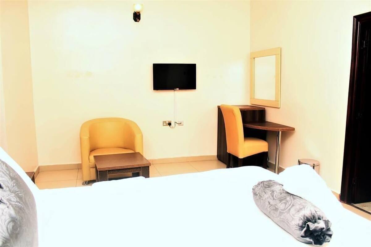 A hotel room with a bed, a desk, a chair, a TV, and a mirror.