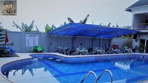 En swimmingpool med en blå kakelbeklädd kant, ett överbyggt sittområde med stolar och en skylt med poolens regler.