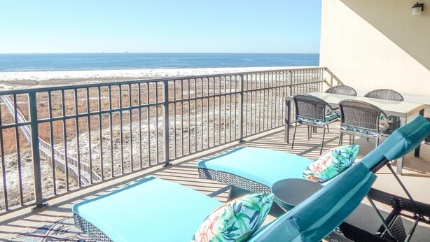 Een balkon met uitzicht op het strand, een tafel met stoelen en ligstoelen met kussens.