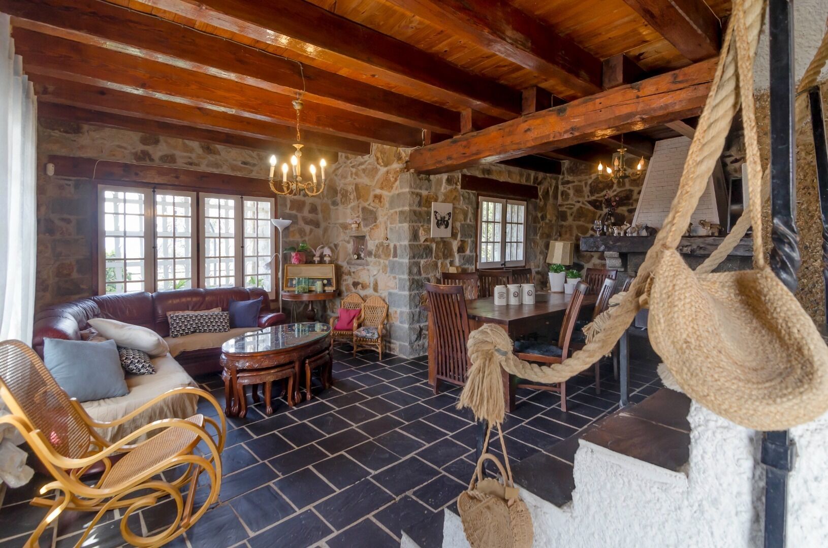 A rustic interior with stone walls, wooden beams, a stone fireplace, a dining area, and a hammock.