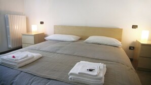 Una habitación de hotel con una cama grande, dos mesitas de noche y un calentador fijado a la pared.