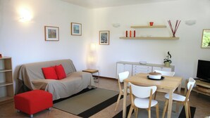 Una sala moderna con un sofá, reposapiés y una mesa de comedor con sillas. Cuenta con una zona de cocina con mostrador y armarios.