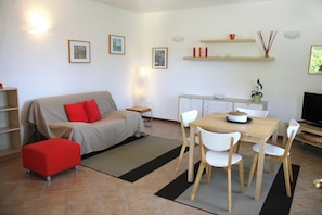 Ein modernes Wohnzimmer mit Sofa, Hocker und Esstisch mit Stühlen. Es gibt eine Küchenzeile mit Arbeitsfläche und Schränken.