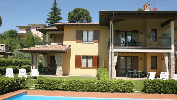 Una casa de dos pisos con piscina, mobiliario exterior y un balcón.