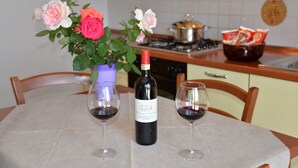 A dining table with a bottle of wine and two glasses, a vase with flowers, and a kitchen in the background. - Two-room Apartment for 3 People With Kitchen and Private Bathroom (Arezzo)