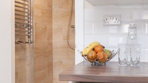 Un comptoir de cuisine avec un panier de fruits contenant des bananes, des oranges et des pommes, deux verres transparents et une prise électrique blanche.