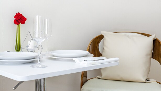 Une table à manger dressée avec des assiettes, des verres et un vase contenant une fleur rouge.
