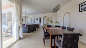 Un espace repas avec une longue table, des chaises et un lustre. On aperçoit un canapé et une table à manger au fond.