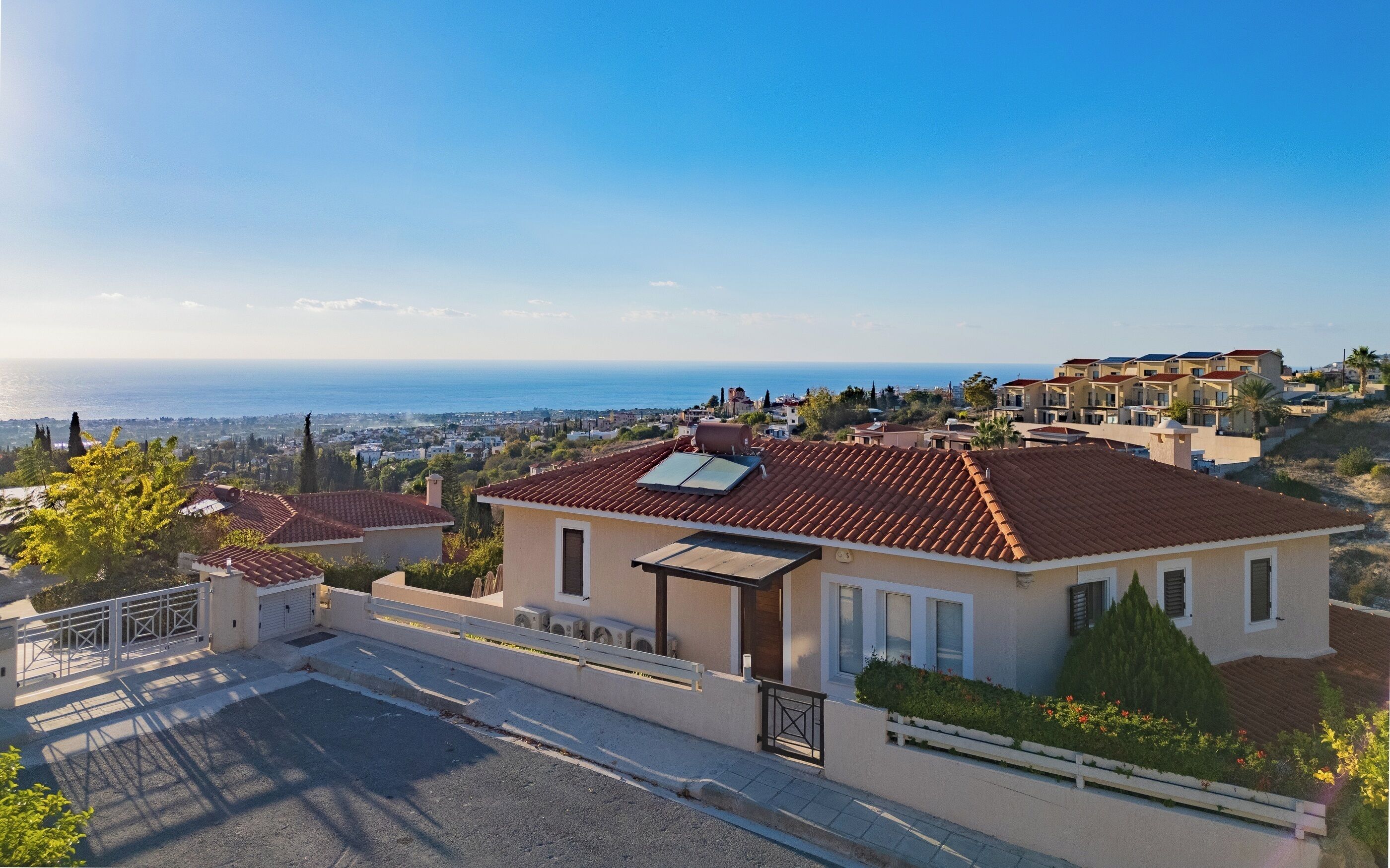 A residential building with a red-tiled roof, a solar water heater, and a view of the sea.