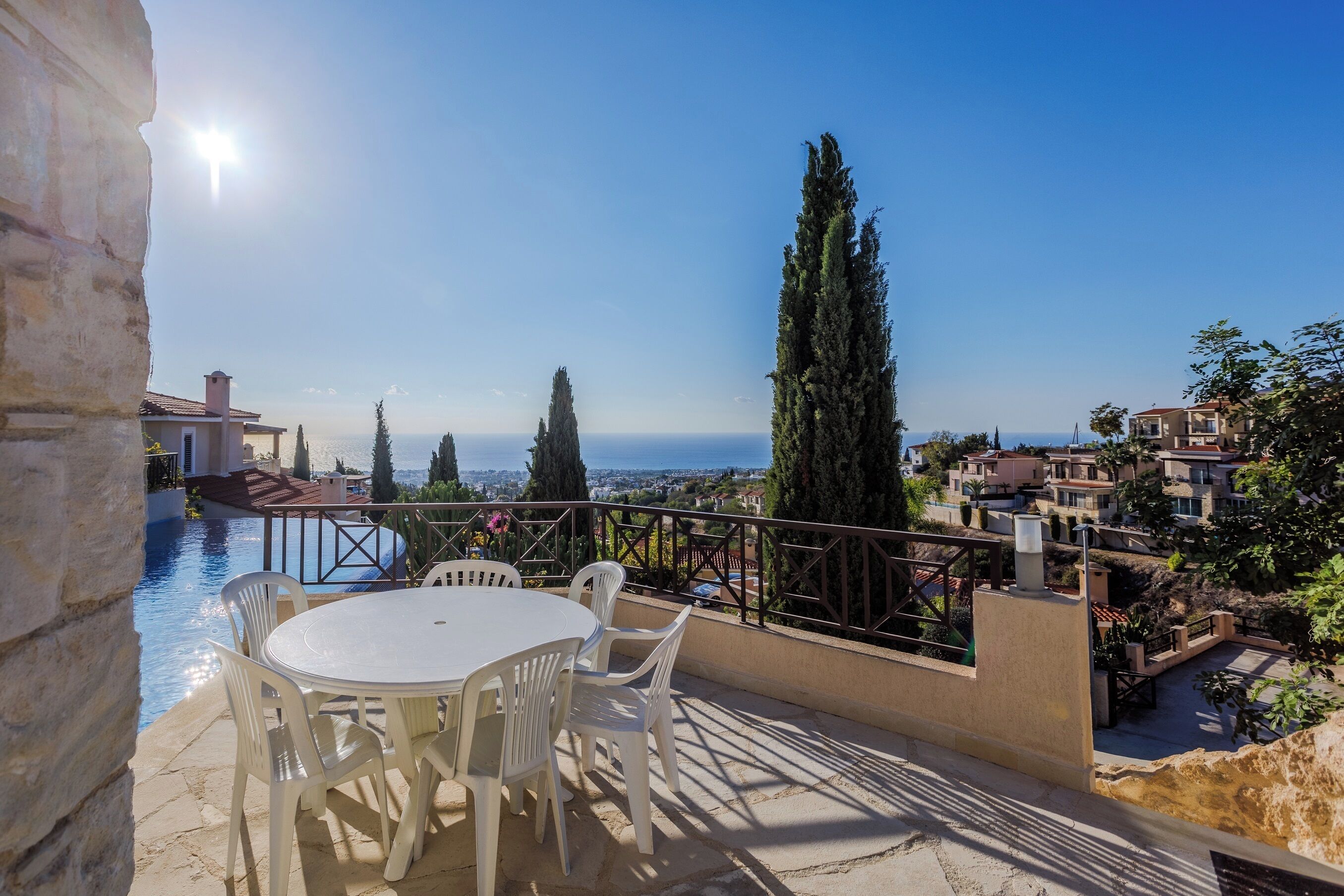 A terrace with a table and chairs overlooking a pool and a coastal view.