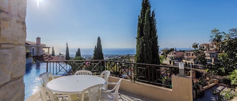 A terrace with a table and chairs overlooking a pool and a coastal view.