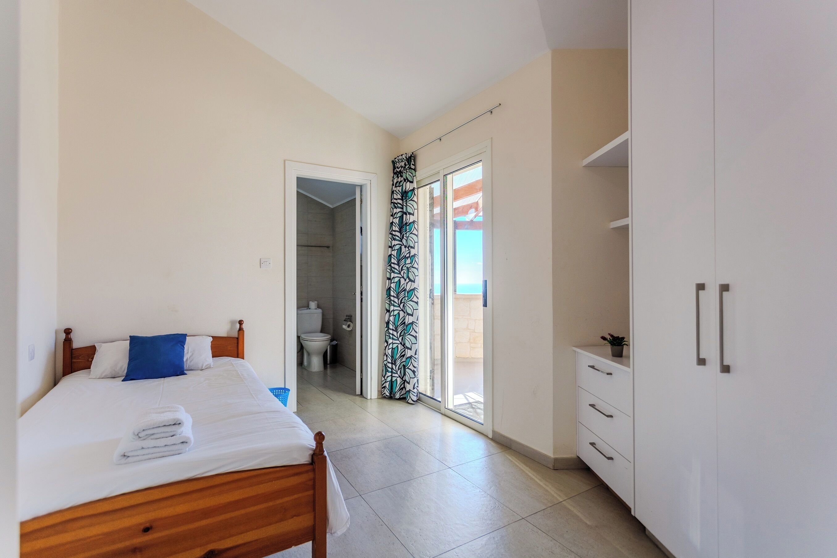 Une chambre à coucher avec un lit, une armoire et une salle de bain visible à travers une porte ouverte.