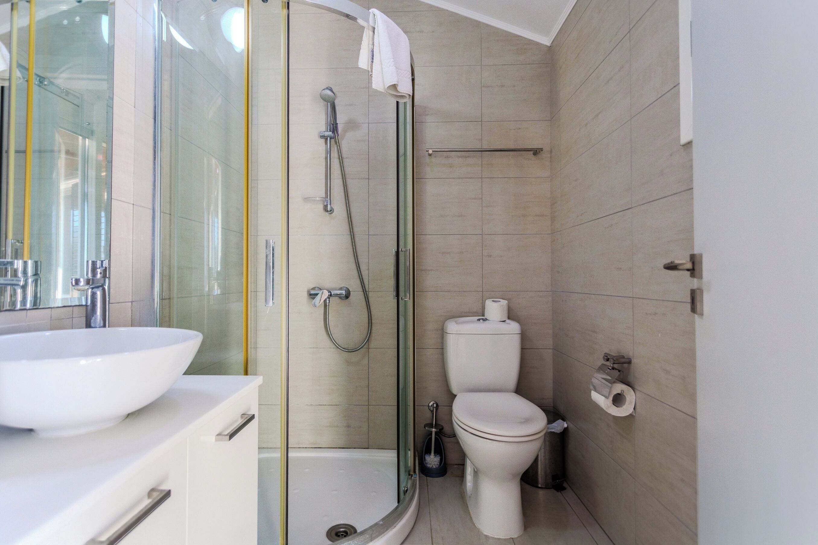 Ein modernes Badezimmer mit Duschkabine aus Glas, einer weißen Toilette und einem großen, weißen Waschbecken.
