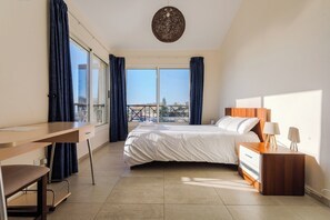 A hotel room with a bed, a desk, a chair, a nightstand, and a view of the city. - Resitour - Perneri Villas (Tala)