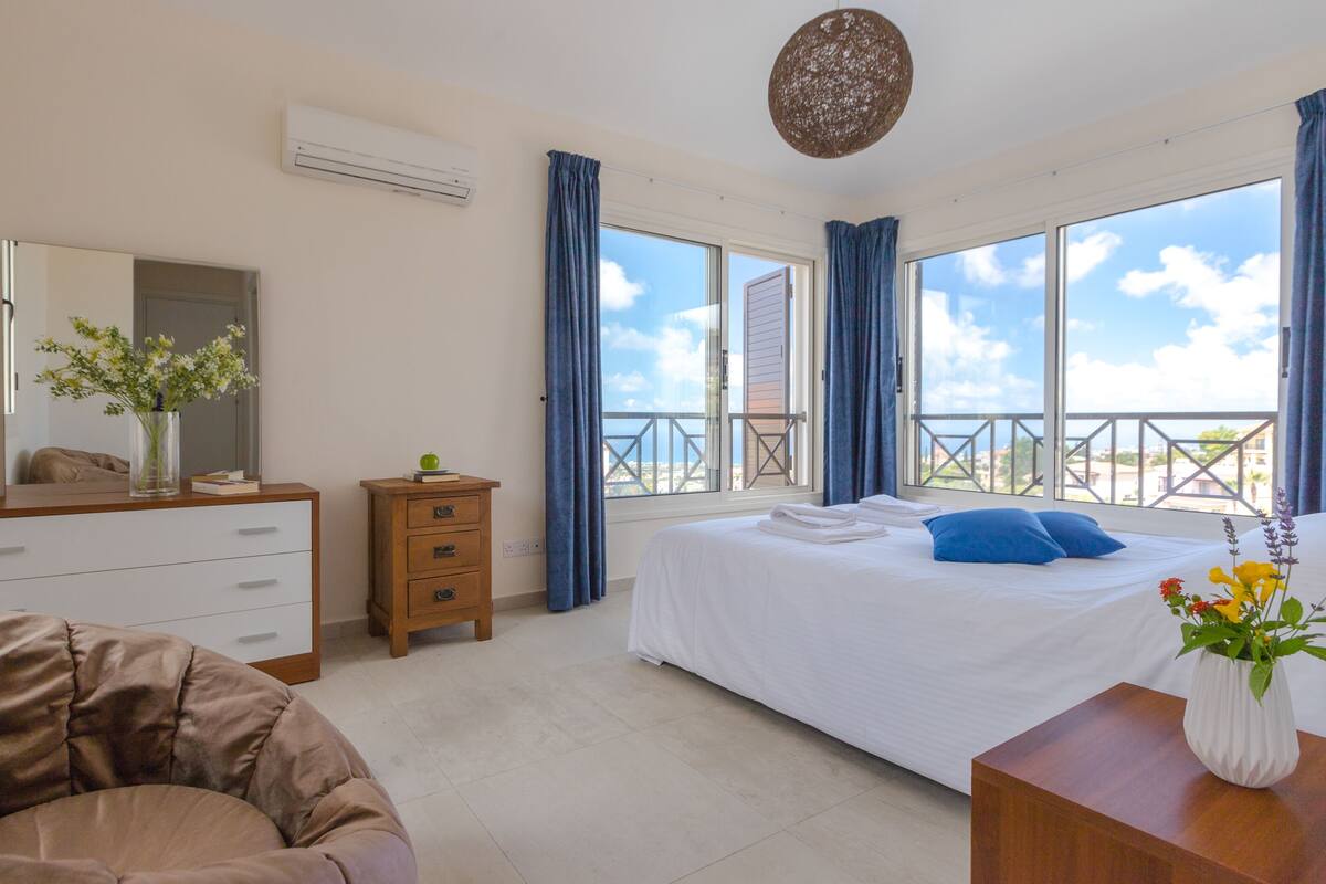 A bedroom with a bed, a dresser, a chair, a bedside table with a vase, and a balcony with a railing.