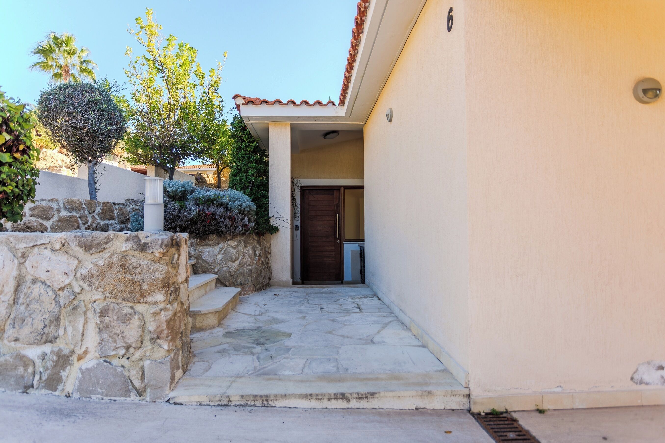 A stone staircase leading to a wooden door, with a stone wall and vegetation on the left.