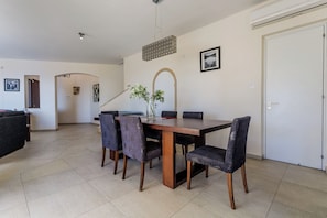 A dining area with a wooden table and six chairs, a vase with flowers, and a framed picture on the wall. - Resitour - Perneri Villas (Tala)