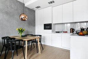 Une cuisine moderne avec des meubles blancs, un four noir et une table à manger en bois, assortie de chaises noires.