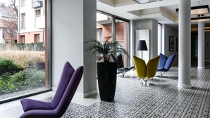A modern lobby with large windows, a potted plant, and colorful chairs. - Otium Old Town Harmonica (Kraków)