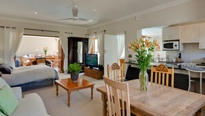 A spacious living area with a sofa, a wooden dining table, a TV, and a kitchen in the background. - Lavender Cottage 2 Double Bedrooms 2 Bathrooms both on suite Beautiful Views (Cape Town)