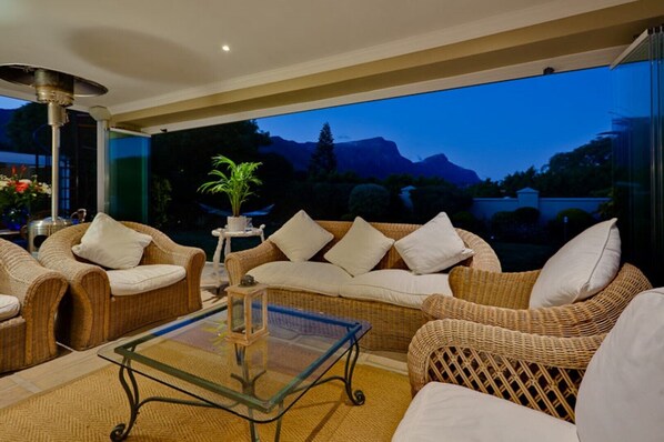 Relax in a serene lounge area with wicker sofas, armchairs, and a glass coffee table, surrounded by a mountain view.