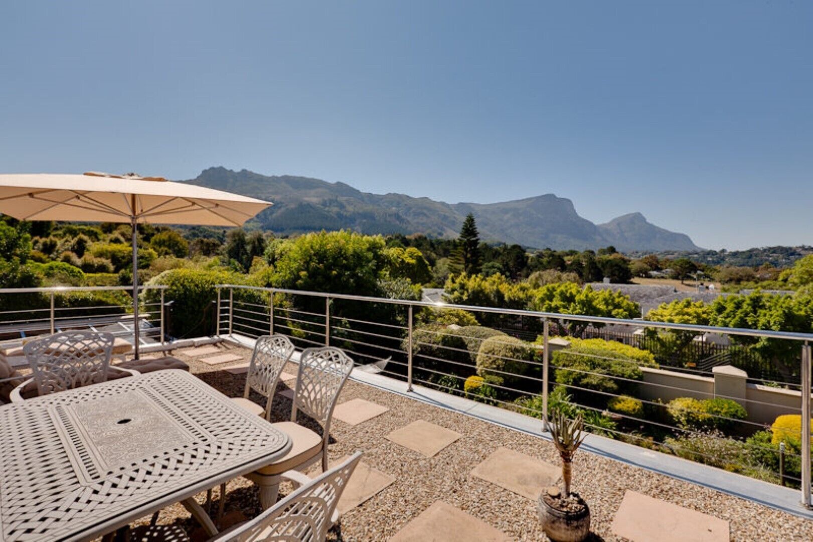 Une terrasse extérieure avec une table et des chaises, une rambarde en métal et une vue sur les montagnes et la verdure.