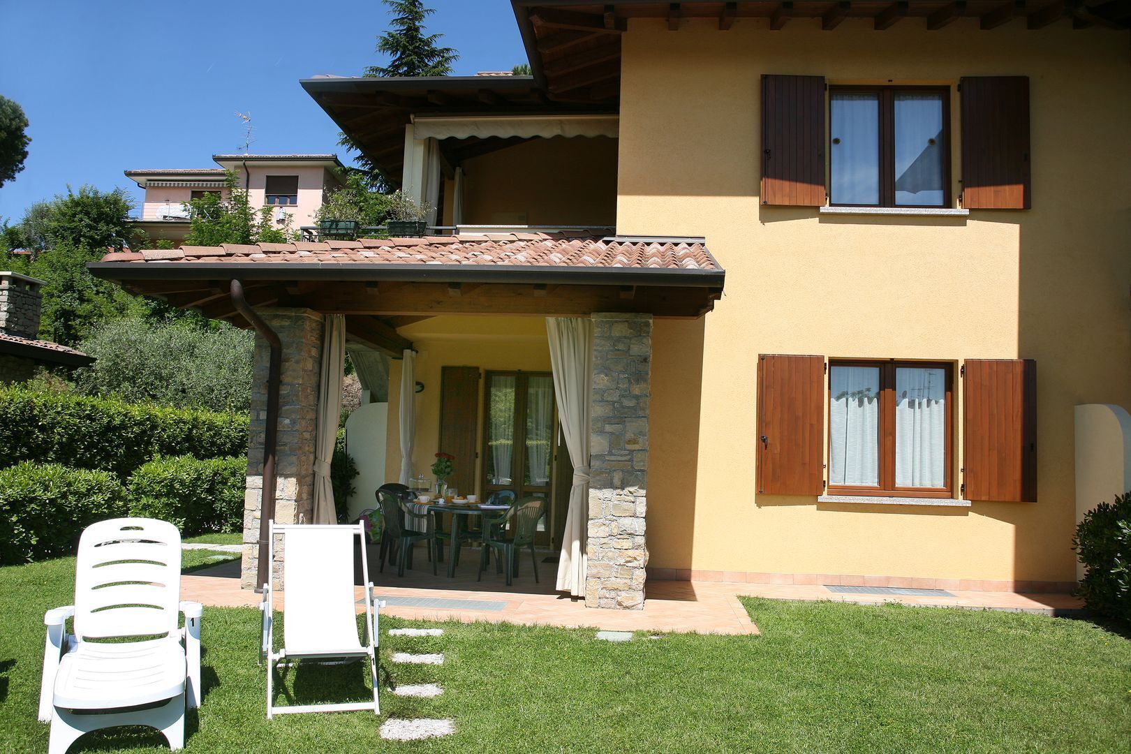 Una casa de dos pisos con un patio, mobiliario exterior y un muro de piedra.
