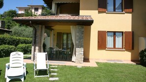 Une maison à deux étages avec un patio, un espace salon extérieur et un mur en pierre.