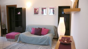 Un salon moderne avec un canapé, une table basse sur laquelle est posé un vase rempli de fleurs séchées, une bibliothèque et des œuvres d’art accrochées au mur.