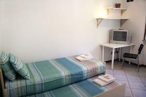 Pieni huone, jossa on yksi sänky, työpöytä, jossa on televisio, ja tuoli.