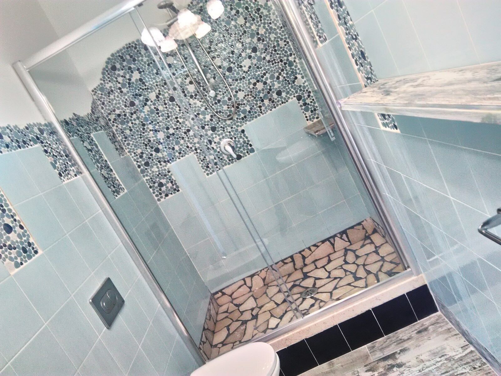Un baño con zona de ducha, paredes con azulejos y una pared de acento de piedra.