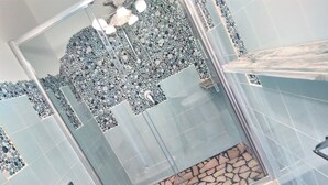 A bathroom with a shower area, tiled walls, and a stone accent wall. - Room-versomare - Room Maestrale Extra Be (Polignano a Mare)