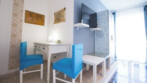 A room with a white desk, two blue chairs, a world map, and a TV on a white shelf. - Room-versomare - Room Maestrale Extra Be (Polignano a Mare)