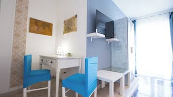 Una habitación con un escritorio blanco, dos sillas azules, un mapa mundial y una televisión sobre una estantería blanca.