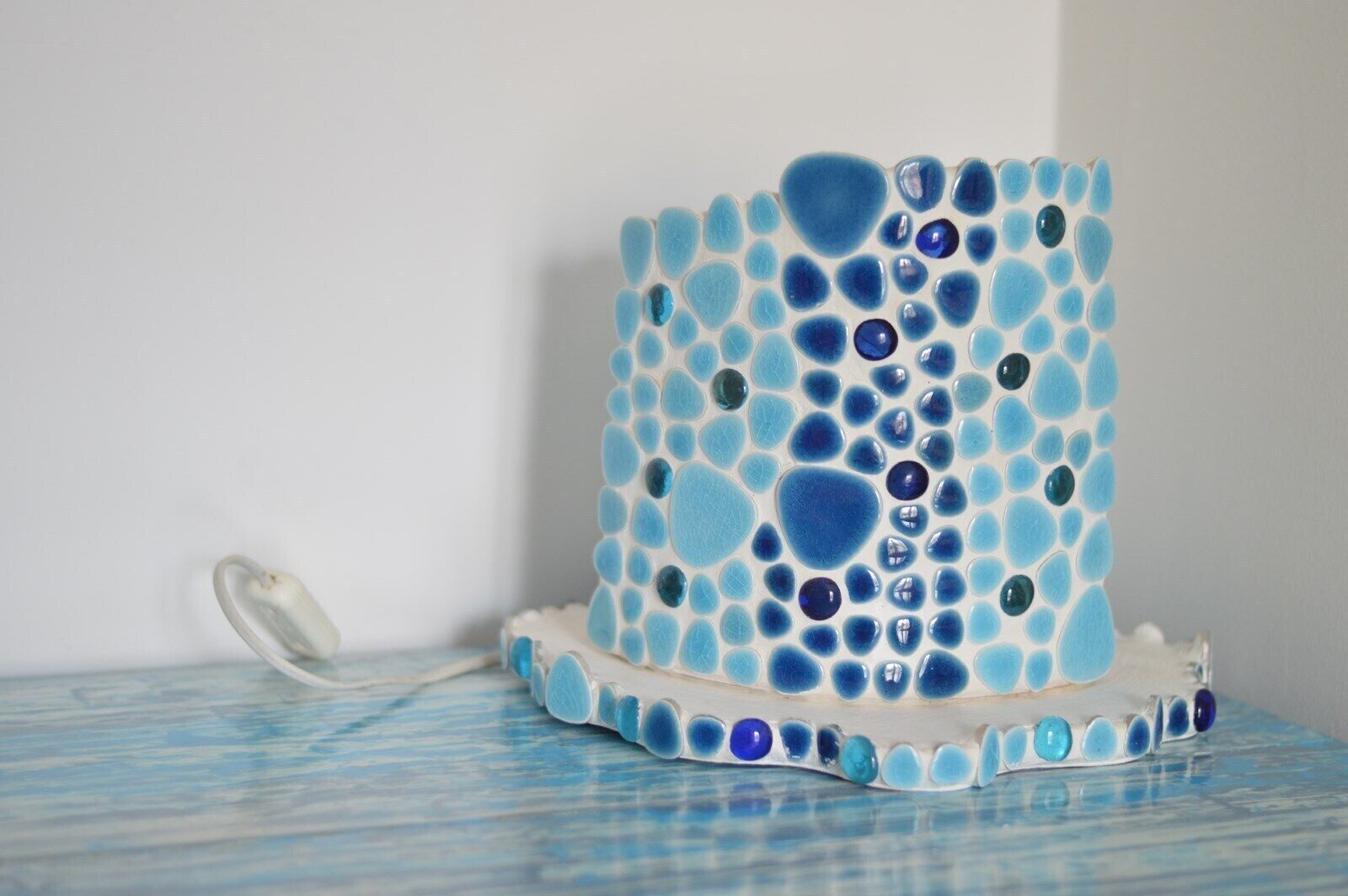 Un objeto decorativo con un diseño de mosaico, posiblemente una obra de arte o una escultura, sobre una superficie con un estampado azul y blanco a rayas.