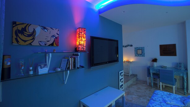 Un salon moderne avec un mur d’accent bleu, un téléviseur à écran plat, une table basse en verre, une table d’appoint blanche et un couvre-lit à motifs.