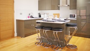 A modern kitchen with a central island, bar stools, stainless steel appliances, and wooden cabinetry. - The Elm Serviced Apartments (Camberley)