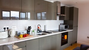 A modern kitchen with stainless steel appliances, a built-in oven, and a large window providing natural light. - The Elm Serviced Apartments (Camberley)