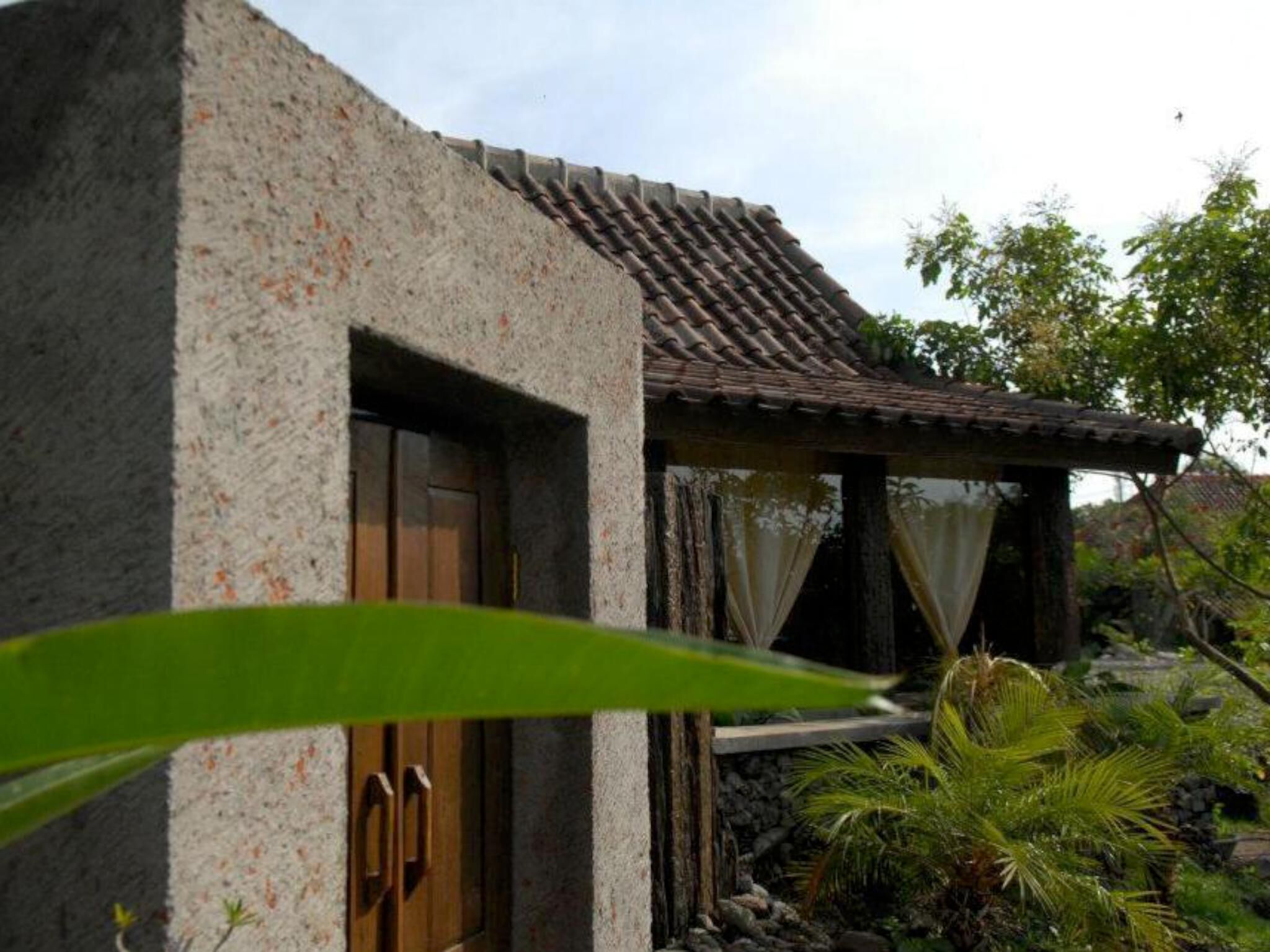 A house with a stone facade, a tiled roof, and a small porch with a curtain.