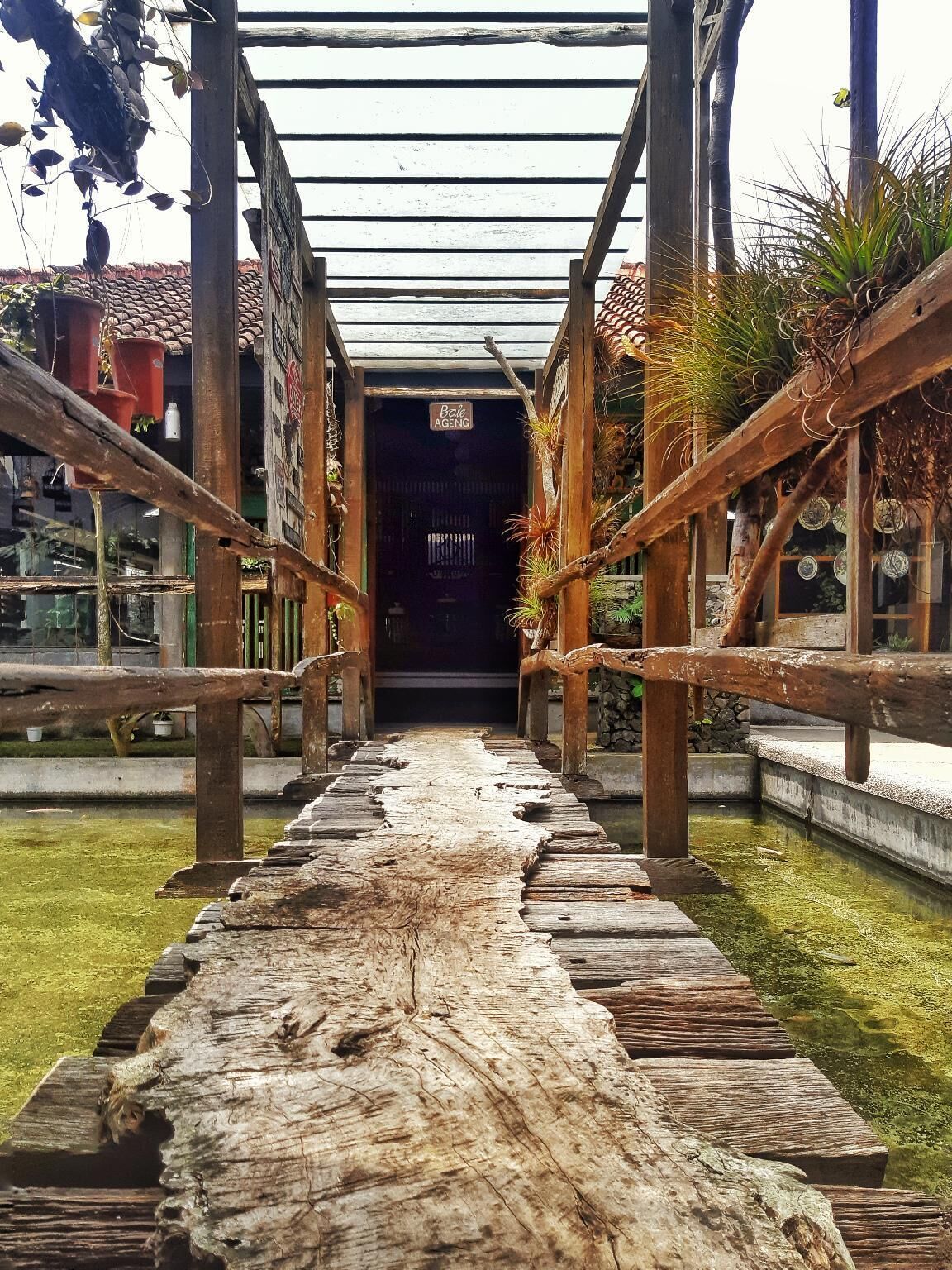 A wooden pathway leading to a building with a sign reading "Bale Aeng."