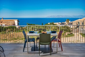 Una terraza con una mesa preparada para dos, con vista al mar y edificios y montañas a lo lejos.
