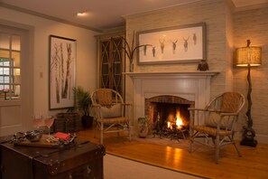 Un salon chaleureux avec une cheminée, des fauteuils en osier et une grande œuvre d’art encadrée au-dessus.