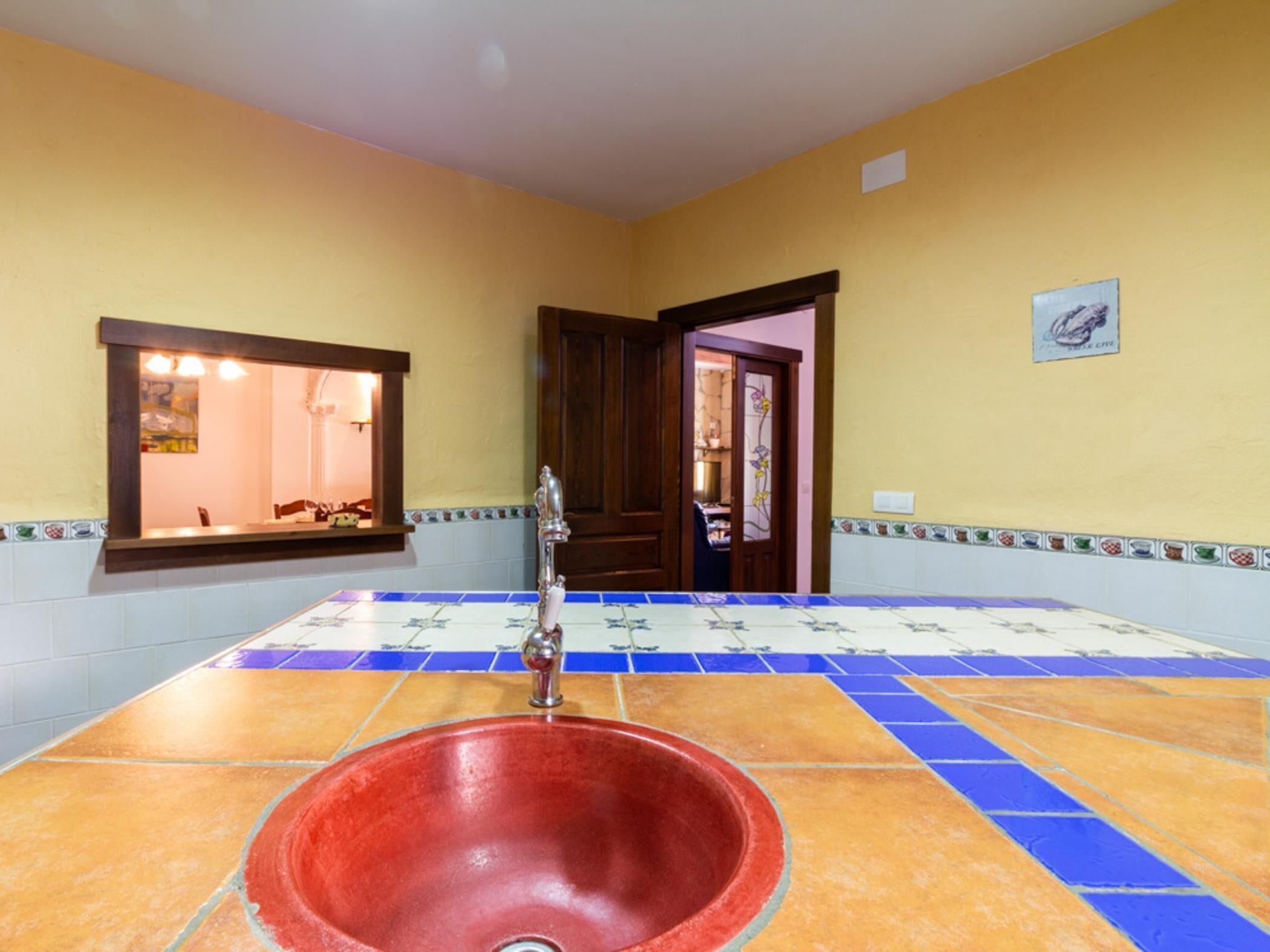 A bathroom with a red sink, a mirror, and a door leading to another room.