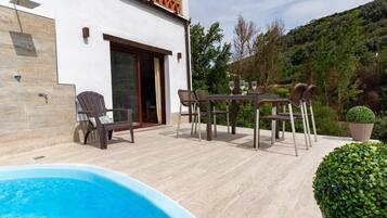 A poolside area with a hot tub, outdoor seating, and a view of a hillside.