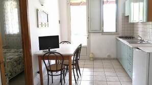 A compact kitchen with a dining table, chairs, a TV, and a small window. - APARTMENT 2 ON GARDEN (UGGIANO LA CHIESA)