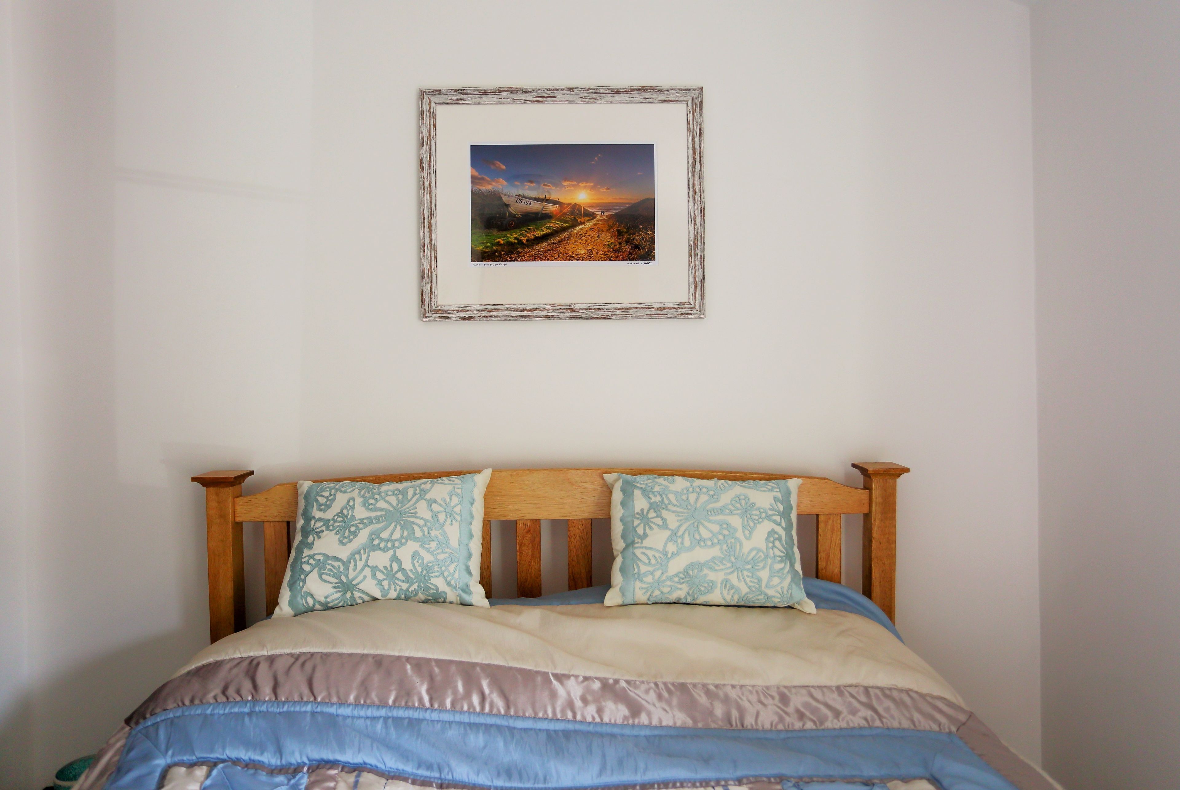 A bedroom with a wooden headboard, a bed with a striped bedspread, and a framed picture of a landscape on the wall.